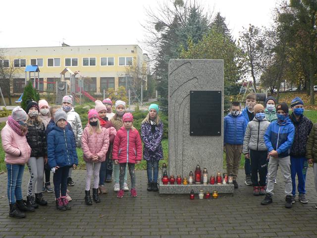Grupa dzieci przy pomniku Stalag 319. W tle budynek szkoły.