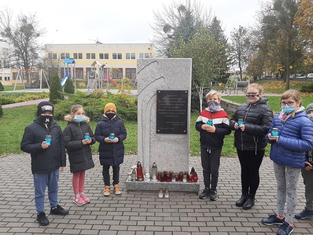 Grupa uczniów ze zniczami w dłoniach przy pomniku Stalag 319. W tle budynek szkoły.