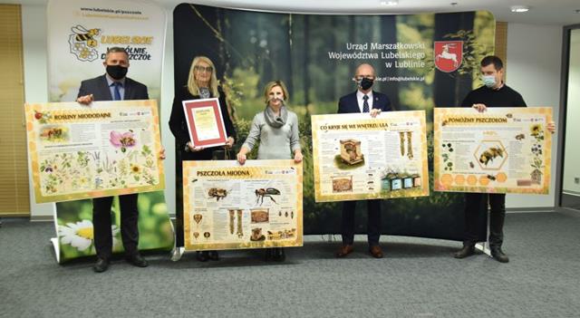 Zdjęcie przedstawia panią dyrektor  podczas odbioru  certyfikatu wieńczącego zrealizowanie edukacyjnego projektu o pszczołach. Pozostałe osoby trzymają plansze edukacyjne związane tematycznie z pszczołami.