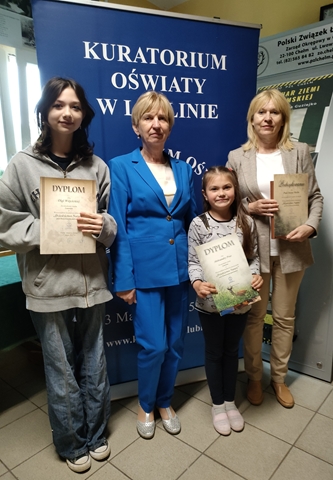 Dwoje dzieci z dyplomami. Przy dzieciach stoją dwie panie.