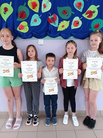 Zdjęcie przedstawiające pięcioro uczniów prezentujących dyplomy na tle udekorowanej tablicy.