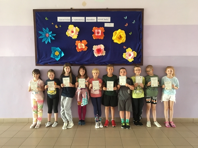 Zdjęcie przedstawiające uczniów prezentujących dyplomy na tle udekorowanej tablicy.