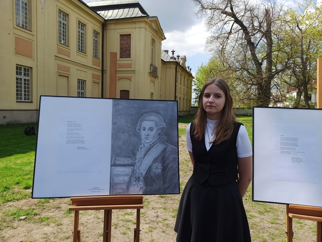 Zdjęcie przedstawia Maję Kusz z jej pracą plastyczną w pobliżu pałacu.