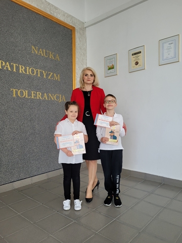 Pani Dyrektor stoi z laureatami konkursu „Kangur Matematyczny”. Dziewczynka i chłopiec trzymają dyplomy i nagrody.