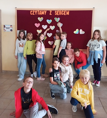 Zdjęcie przedstawiające grupę uczniów na tle tablicy z napisem ,,Czytamy z Sercem’’ oraz wycięte z papieru serca.