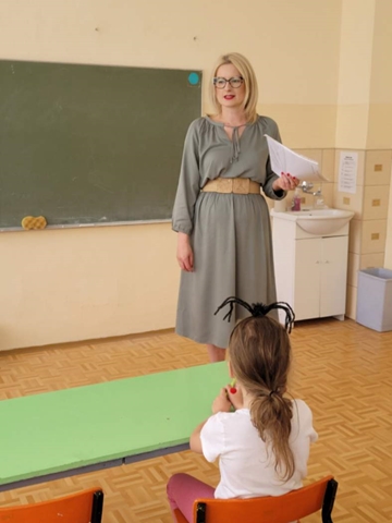 Pani wicedyrektor w sali lekcyjnej rozpoczyna eliminacje konkursowe. Przy pierwszej ławce siedzi dziewczynka.
