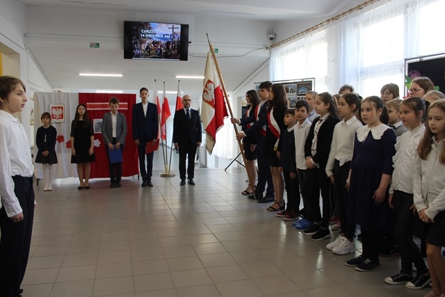 Zdjęcie przedstawiające uczniów stojących w holu szkoły podczas uroczystego apelu.