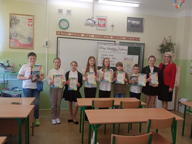 Zdjęcie przedstawia ośmiu laureatów  konkursu „Zdrowa ortografia” z Panią Dyrektor w sali lekcyjnej. Uczniowie trzymają dyplomy i nagrody.