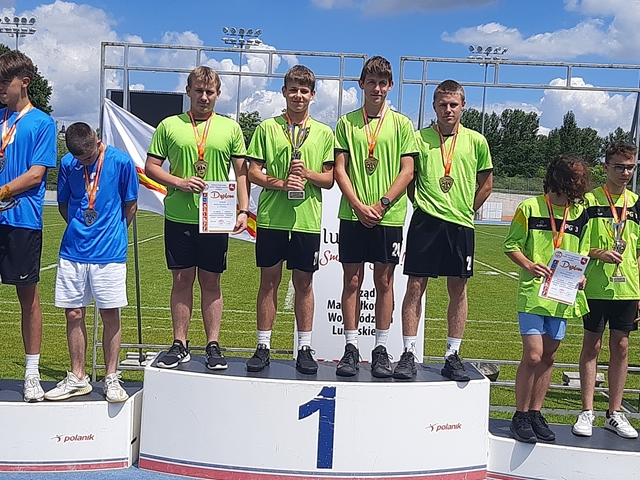 Zdjęcie przedstawiające czterech uczniów na podium. Jeden z uczniów trzyma puchar, drugi dyplom, wszyscy eksponują medale. 