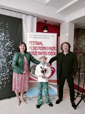 Uczeń w towarzystwie jurorów trzyma nagrodę zdobytą w  XII Finale Festiwalu Polskiej Piosenki o Miłości. Statuetka ma kształt róży.  