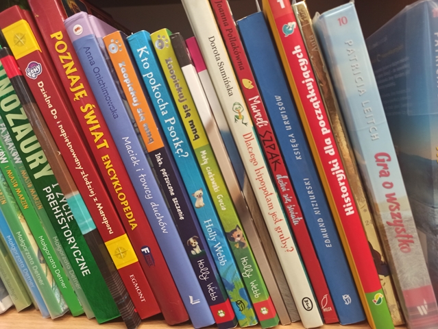 Na półce widzimy kilkanaście różnorodnych książek. Akcję „Kwiatek za książkę” przeprowadza biblioteka szkolna.