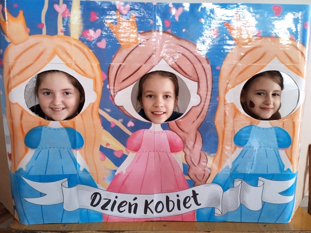 Zdjęcie przedstawia trzy uczennice pozujące do zdjęcia w foto budce z okazji Dnia Kobiet.