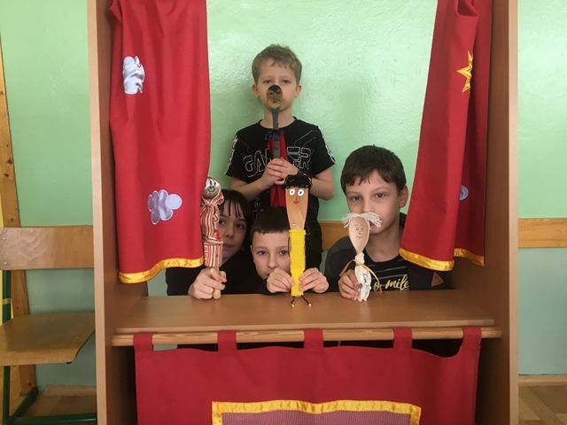 Zdjęcie przedstawia niewielką grupę uczniów w kąciku teatralnym. Chłopcy prezentują kukiełki wykonane z drewnianych łyżek.