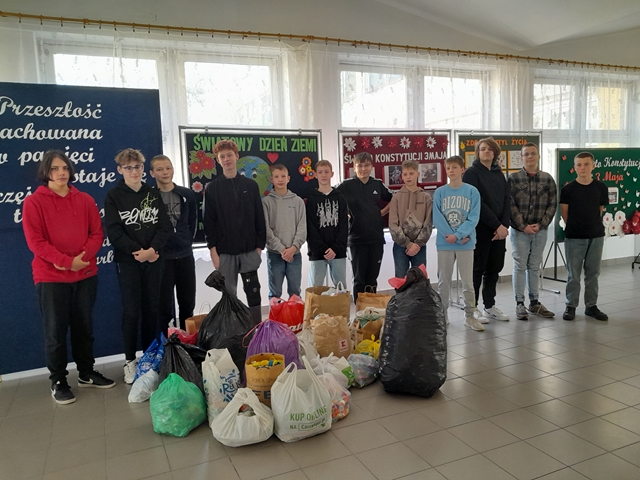 Grupa chłopców stojących na korytarzu szkolnym. Przed nimi leżą worki z zebranymi zakrętkami.