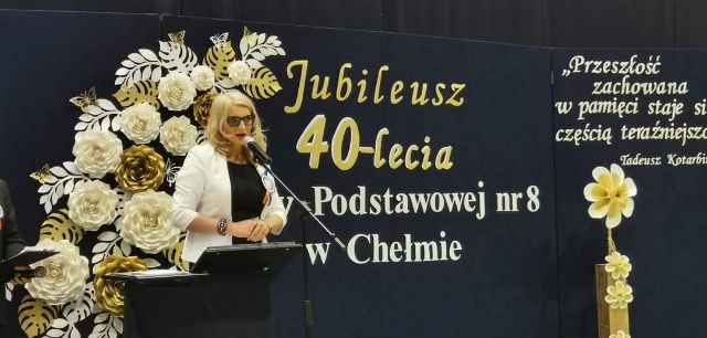 Zdjęcie przedstawia Panią Dyrektor na tle dekoracyjnej tablicy w trakcie przemówienia z okazji Jubileuszu 40-lecia Szkoły Podstawowej nr 8 w Chełmie. 