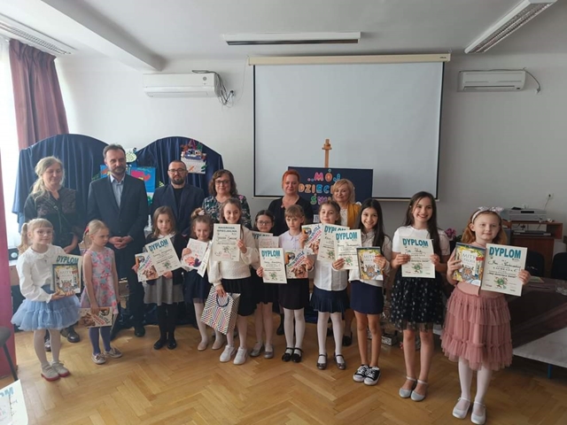 Zdjęcie przedstawia uczniów prezentujących dyplomy i nagrody za udział w konkursie recytatorskim. Za dziećmi stoją organizatorzy przedsięwzięcia i zaproszeni goście.
