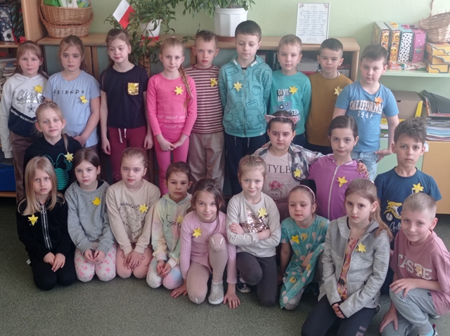 Grupa uczniów w klasie. Każde dziecko ma przypięty do ubrania żonkil.